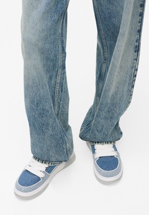 Modré riflové tenisky s bielymi šnúrkami a sivými podrážkami. Zničené modré široké nohavice majú viditeľné švy a voľný strih.