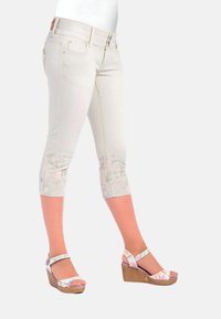 Beige Capri-Hosen mit floralem Muster am Saum, aus weichem Stoff. Kombiniert mit mehrfarbigen Keilsandalen und verstellbaren Riemen.