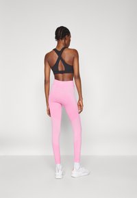 Bra sportivo nero con design a schiena incrociata. Leggings rosa con un motivo testurizzato e vita alta, dotati di pannelli a contrasto. Scarpe da ginnastica bianche.