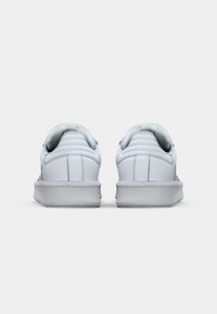 White sneakers with a smooth leather upper, padded collar, and textured rubber sole. Features minimal design and no notable accents.