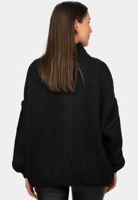 Zwarte gebreide trui met een hoge nek, oversized pasvorm, geribbelde boorden en textuurstof, van achteren getoond. Geen zichtbare patronen of accenten.