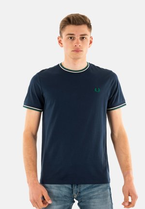 Camiseta de algodón de color azul marino con mangas cortas, que presenta un cuello y puños a rayas verdes y blancas, y un pequeño logo bordado en el pecho.
