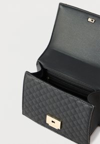 Μαύρη δερμάτινη τσάντα με υφή και καπιτονέ σχέδιο, ανοιχτό καπάκι που αποκαλύπτει ευρύχωρο εσωτερικό και χρυσό ορθογώνιο κούμπωμα μπροστά.