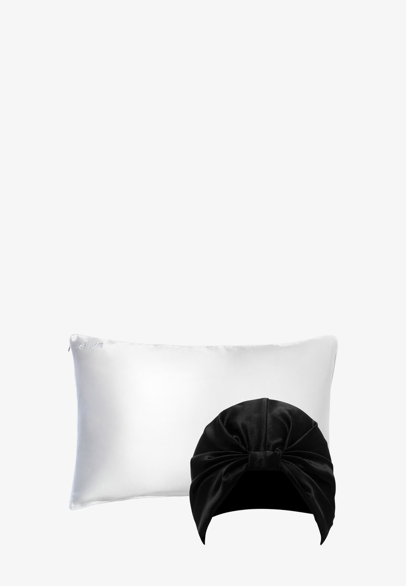 Taie d'oreiller rectangulaire en soie blanche et turban de sommeil en velours noir positionnés devant sur fond gris