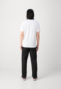 Hvid bomulds t-shirt med korte ærmer, parret med sorte cargo bukser med sidelommer, synlige sømme og en afslappet pasform.