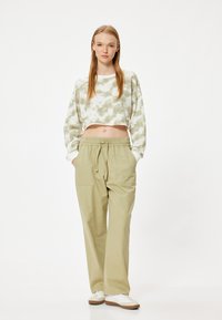 Hellgrünes Batik-Cropped-Sweatshirt und hellolivfarbene weite Hosen mit verstellbarem Bund. Das Model posiert mit den Händen in den Taschen.