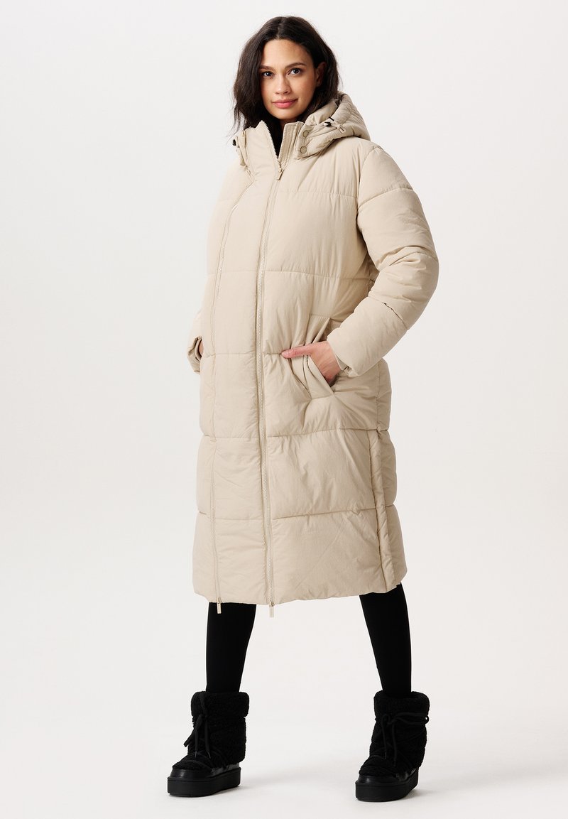 Beige vadderad lång kappa med en åtsittande huva, dragkedjestängning och sidofickor. Bärs över svarta leggings och foderfodrade ankelstövlar.