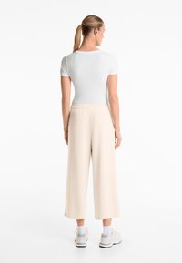 Light gray fitted t-shirt with short sleeves paired with loose, light beige cropped trousers, worn with white sneakers and crew socks.