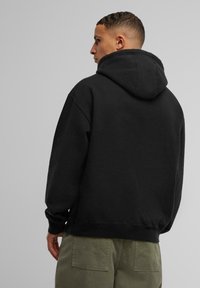 Schwarzer Kapuzenpullover mit geräumiger Kapuze, gerippten Bündchen und Saum, kombiniert mit olivgrünen Hosen. Weiche Textur, lässiges Design.