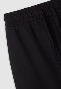 Czarne dresy mają elastyczny pas, sznurki i miękką fakturę, z widocznymi szwami wzdłuż krawędzi.