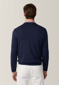 Maglione blu navy con una texture liscia e colletto a coste. Dettaglio delle maniche a righe bianche e rosse visibile al polso.