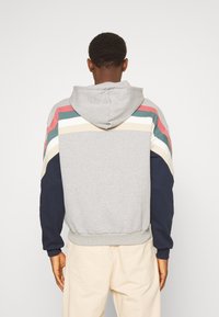 Felpa grigia con maniche color block in rosso, verde, beige e blu navy. Presenta un cappuccio con cordino e polsini e orlo a coste.