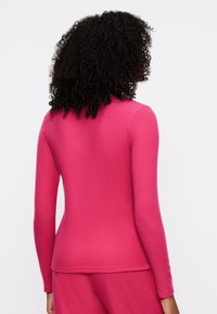 Aansluitend shirt met lange mouwen in felroze gebreid materiaal met een gladde textuur, voorzien van een eenvoudig ontwerp aan de achterkant en een rond decolleté.