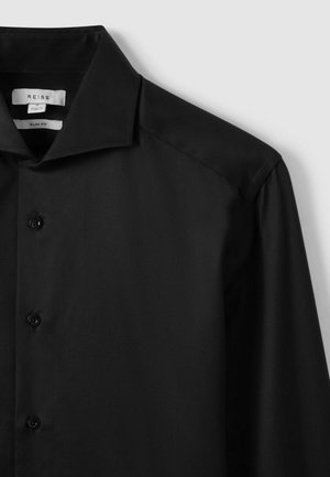 Zwarte slim-fit blouse met een strak ontwerp, gladde textuur, knoopsluiting en een gestructureerde kraag. Labels zijn zichtbaar binnen de kraag.