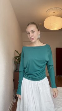 Mėlynos spalvos ilgas rankovės palaidinė su plačiu iškirpimu, krentanti dizaino forma, derinama su balta, tekstūruota, iki kulkšnių ilgio sijonu. Lengva, orinė medžiaga su laisvu siluetu.