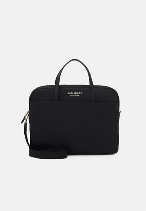 Sac pour ordinateur portable noir Kate Spade New York avec doubles poignées, poche avant, fermeture éclair et bandoulière amovible sur fond blanc.