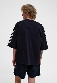 Zwarte oversized t-shirt met een ronde halslijn en witte diagonale strepen op de mouwen. Het model draagt bijpassende zwarte shorts.