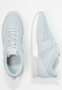 Baskets athlétiques bleu clair avec un mélange de matériaux lisses et texturés, dotées d'un système de laçage et d'une semelle blanche épaisse.