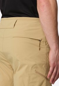 Beige hiking pants with a smooth texture, featuring a side zippered pocket, flat waistband, and reinforced stitching at the seams.