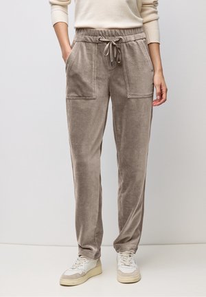 Pantalon jogger beige en velours côtelé avec poches plaquées devant, porté avec un pull crème et des baskets blanches. Mains dans les poches.