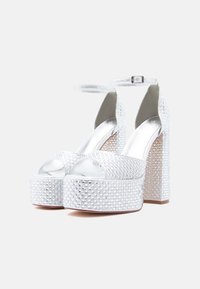 Stříbrné platformové podpatky s povrchem pokrytým kamínky, otevřená špička, zapínání kolem kotníku a robustní podpatky. Hladký kovový vnitřní povrch.