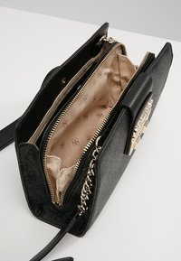 Sort struktureret håndtaske med skinnende guldhardware. Tekstureret ydre, med lynlåslommer. Inder i beige stof med subtilt logo-mønster.