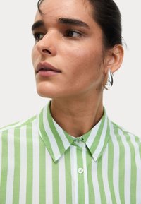 Groen en wit gestreepte button-up shirt met een kraag. Heeft een gladde katoentextuur en ronde knopen, gestyled met zilveren druppeloorbellen.