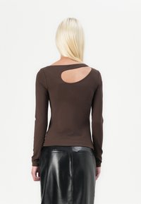 Maglietta marrone a maniche lunghe con un'apertura rotonda sulla schiena, realizzata in materiale morbido. Indossata con una gonna di pelle nera, caratterizzata da una finitura elegante.