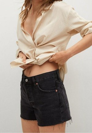Camisa a rayas beige, anudada en la cintura, combinada con pantalones cortos de mezclilla negros de cintura alta con dobladillos deshilachados y detalles en color cobre.