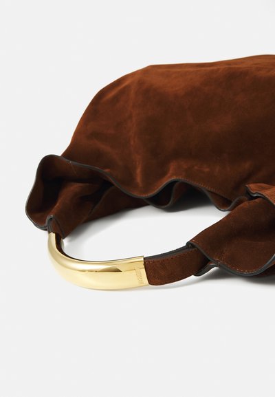 Sac en suède marron avec des bords ondulés et une poignée en métal doré. La poignée présente une courbe douce, mettant en valeur le design du sac.
