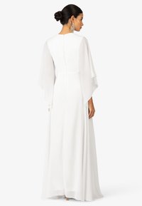 Witte lange jurk met doorschijnende, vloeiende mouwen en een ronde halslijn. Voorzien van een ritssluiting op de rug en een soepele, elegante silhouet.