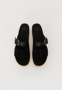 Sorte semskede sandaler med bred stropp, justerbar spenne og en konturert foteng, med en lysebrun gummisåle.