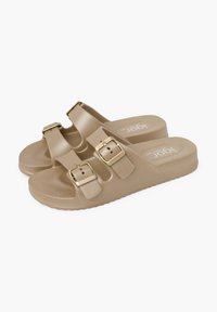 Sandali beige slip-on con due cinghie regolabili, fibbie color oro e suola testurizzata. Suola leggera con motivo antiscivolo per stabilità.