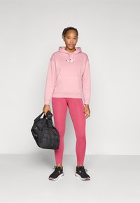 Rosa hettejakke med logo, rosa leggings og svarte treningssko. Svart treningssekk med skulderstropp. Jevnt stoff og formtilpasset design.
