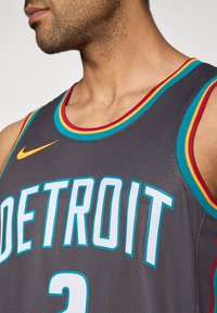 Szürke kosárlabdamez kék, piros és sárga díszítéssel. Nagyméretű "DETROIT" felirattal és Nike logóval. Texturált anyagból, ujjatlan kivitelben.