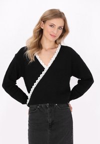 Maglione avvolgente nero con bordino bianco ondulato lungo il collo, caratterizzato da maniche lunghe e un motivo a maglia testurizzato. Abbinato a una gonna nera.