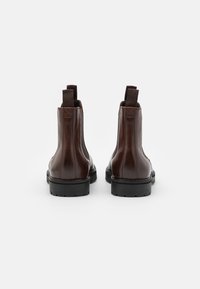 Botas de tobillo de cuero marrón con una textura suave, suela de goma negra y dos hebillas de tela en la parte posterior para ponerlas y quitarlas fácilmente.