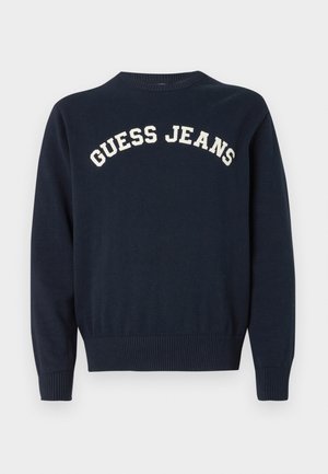 Mornarskoplava plavi pamučni džemper s okruglim izrezom i rebrastim manžetnama, s izvezenim natpisom "GUESS JEANS" u krem boji preko prsa.
