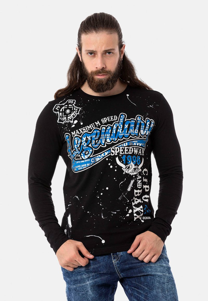 Schwarzes Langarmshirt mit weißem und blauen grafischen Text, Spritzdesign und rundem Halsausschnitt. Getragen mit blauen Jeans.