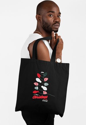 Borsa a tracolla nera con grafiche di lampadine natalizie colorate, con il testo "Buon Natale a Tutti Coca-Cola" in rosso. Materiale in cotone.