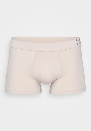 Boxers en coton beige avec une coupe ajustée, dotés d'une ceinture renforcée et d'une ouverture horizontale, décorés de branding subtil sur le côté.