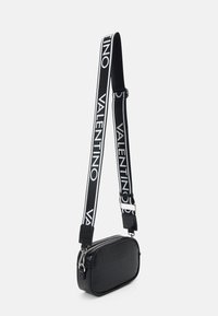 Borsa a tracolla nera con texture a coccodrillo, forma ovale, cerniera argentata e ampia tracolla con la scritta ripetuta "VALENTINO" in bianco.