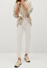 Jersey de color beige con capucha y puños acanalados, combinado con jeans rectos de color claro y zapatillas beige con suelas oscuras.