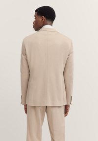 Beige ma�ßgeschneiderte Sakkojacke mit glatter Textur, klassischen Revers und einem Schlitze hinten, von hinten präsentiert.