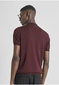 Polo shirt bordeaux à manches courtes avec un col, des poignets côtelés et un petit logo au dos du col. Texture lisse.