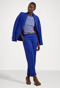 Blazer bleu royal et pantalon assorti, chemise à manches courtes rayée, ceinture en corde naturelle, et sandales à talons épais ; tissu lisse et coupe ajustée.