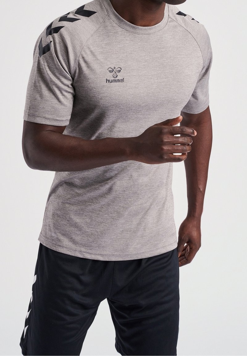 Šedé atletické tričko s černými ramenními akcenty a logem na hrudi, doplněné černými šortkami s bílými bočními detaily.