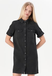 Zwarte denim shirt jurk met korte mouwen, twee borstzakken, knoopsluiting aan de voorkant en een licht gebogen zoom. Zacht, gestructureerd materiaal.