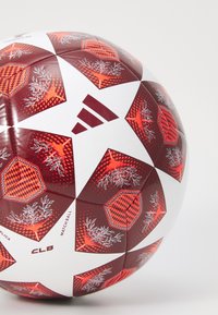 Adidas varžybų kamuolys, turintis sferinę formą, su raudonai baltu spalvų deriniu. Šešiakampės plokštelės su gėlių ir geometriniais raštais, blizgaus paviršiaus.