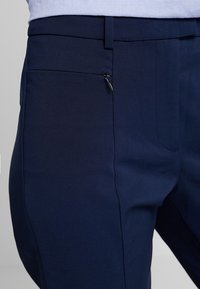 Marintröjor i en slät textil, smal passform, framficka med dragkedja och rena linjer med minimal detaljering.